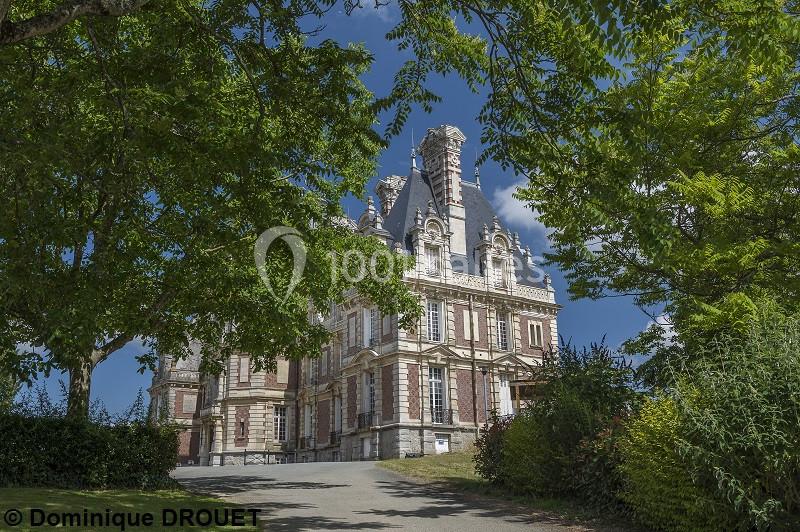 Château en briques et pierres entouré de verdure sous un ciel bleu dégagé.