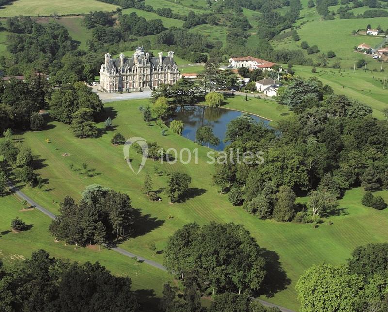 Vue aérienne d'un château entouré de vastes jardins verdoyants, d'un étang et de prairies vallonnées.