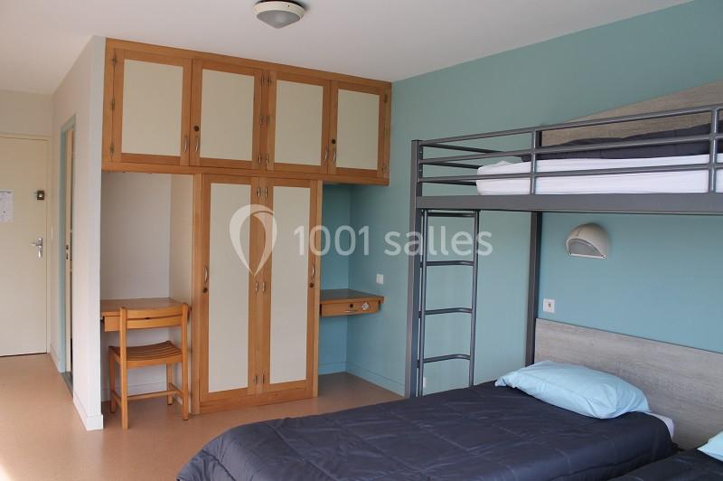 Chambre avec lits superposés, lit simple, armoire en bois, bureau et chaise, murs bleu clair et beige.