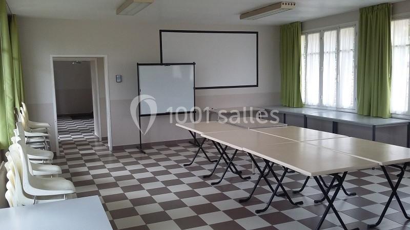 Salle de classe lumineuse avec tables en rangées, chaises alignées, tableau blanc et rideaux verts aux fenêtres.