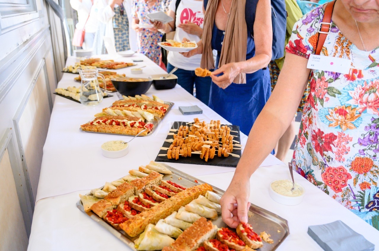 Buffet avec des plateaux de tartes salées, feuilletés et sauces, des personnes se servant en arrière-plan.
