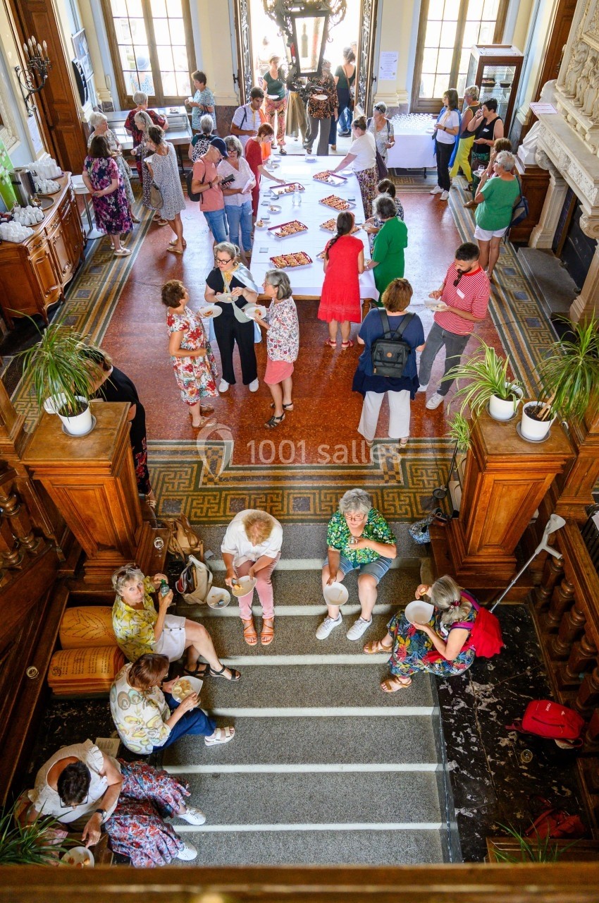 Groupe de personnes échangeant autour d'une table dans un hall lumineux avec escalier et décorations en bois.
