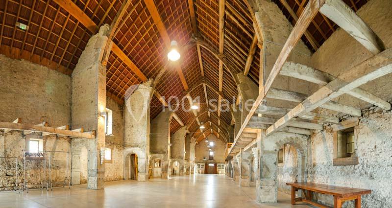 Intérieur d'un bâtiment ancien avec murs en pierre, poutres apparentes et plafond en bois.