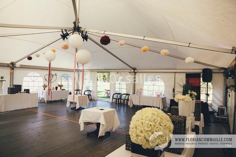 Intérieur d'une tente de réception décorée avec des fleurs suspendues et des tables dressées.