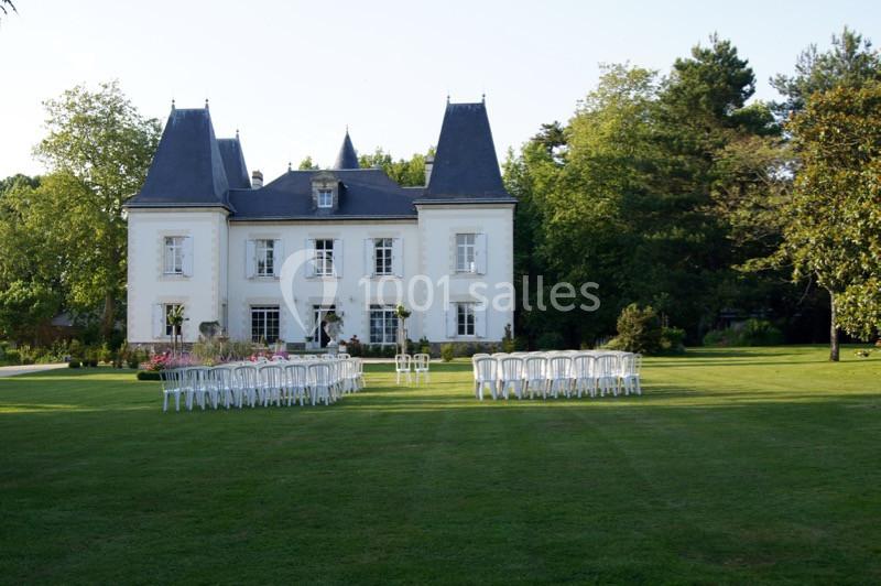 Façade d'un château blanc entouré de verdure, avec des chaises blanches disposées sur une pelouse.