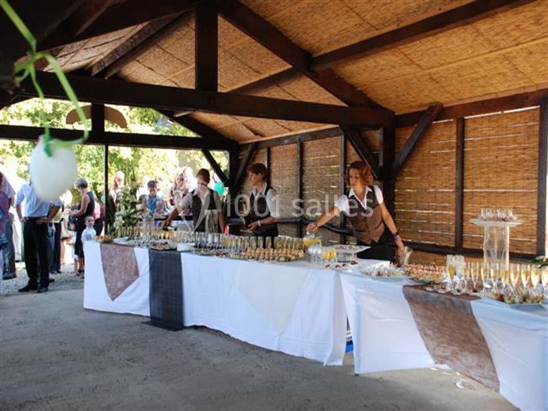 Buffet en extérieur sous un abri en bois, avec des serveuses préparant des boissons et des amuse-bouches.