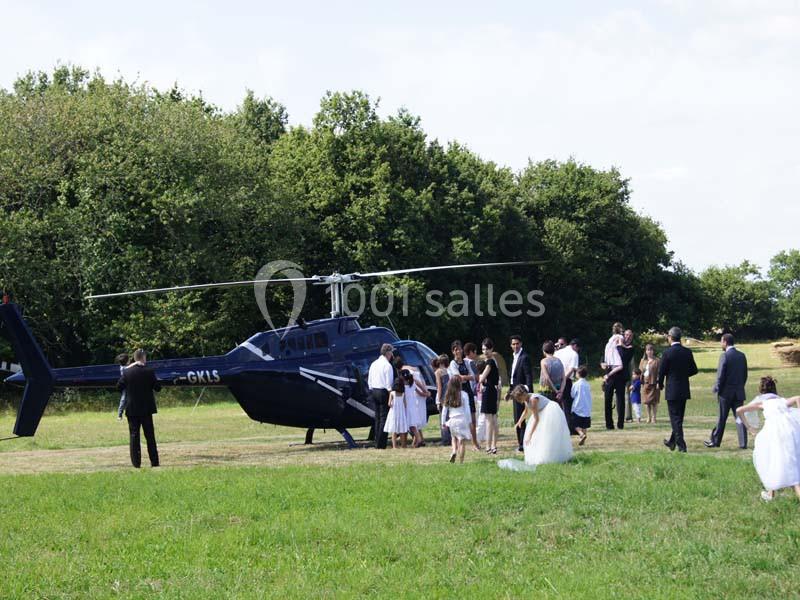 Un groupe de personnes, dont des mariés, se rassemble près d'un hélicoptère posé sur une pelouse.