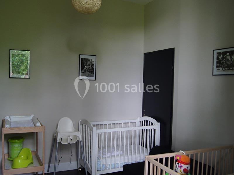 Une chambre d'enfant avec un lit bébé, une table à langer, une chaise haute et des cadres accrochés au mur.