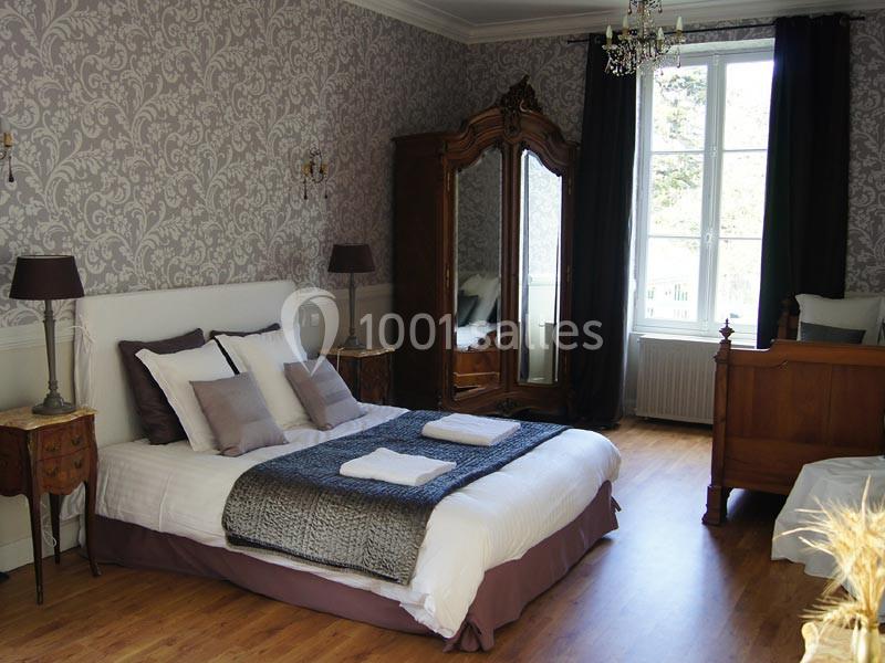 Chambre lumineuse avec lit double, armoire en bois, lit simple, parquet et grande fenêtre avec rideaux sombres.