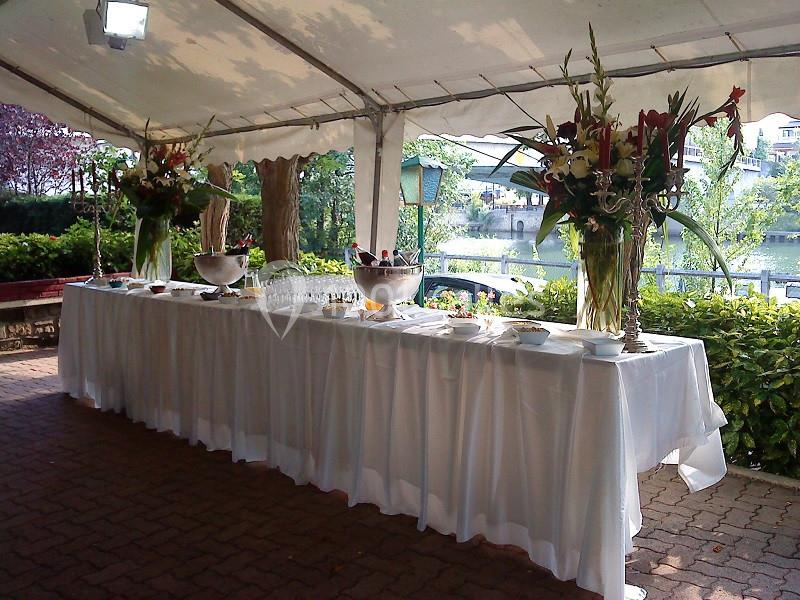 Table de buffet dressée sous une tente, ornée de grandes compositions florales, avec vue sur un espace extérieur verdoyant.
