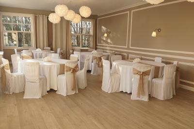 Salle lumineuse avec une grande table rectangulaire dressée, entourée de chaises décorées, parquet clair et fenêtres donnant…