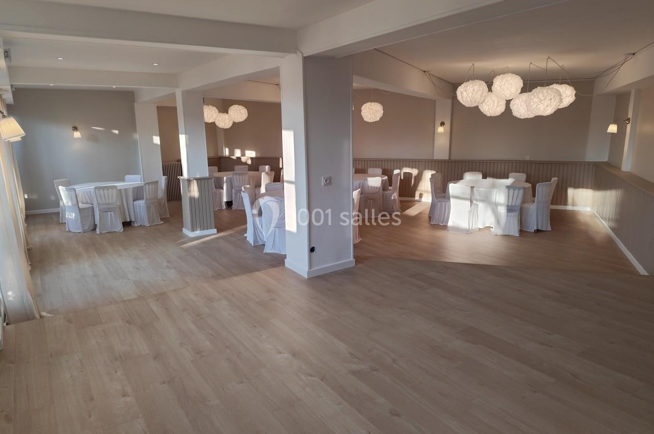 Salle lumineuse avec parquet clair, tables rondes dressées et chaises blanches, éclairée par des suspensions modernes.