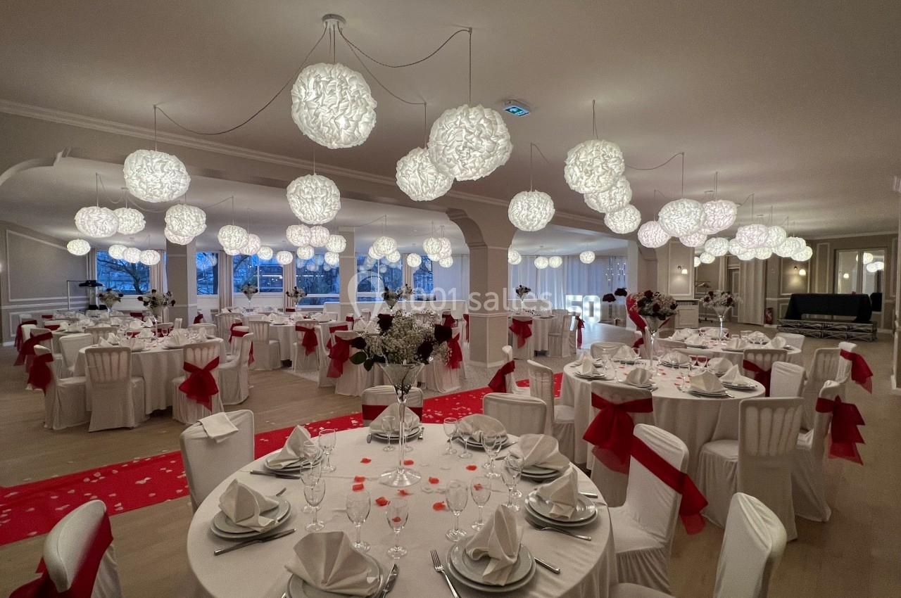 Salle de réception élégamment décorée avec des tables rondes, nappes blanches, chaises ornées de nœuds rouges et éclairage…