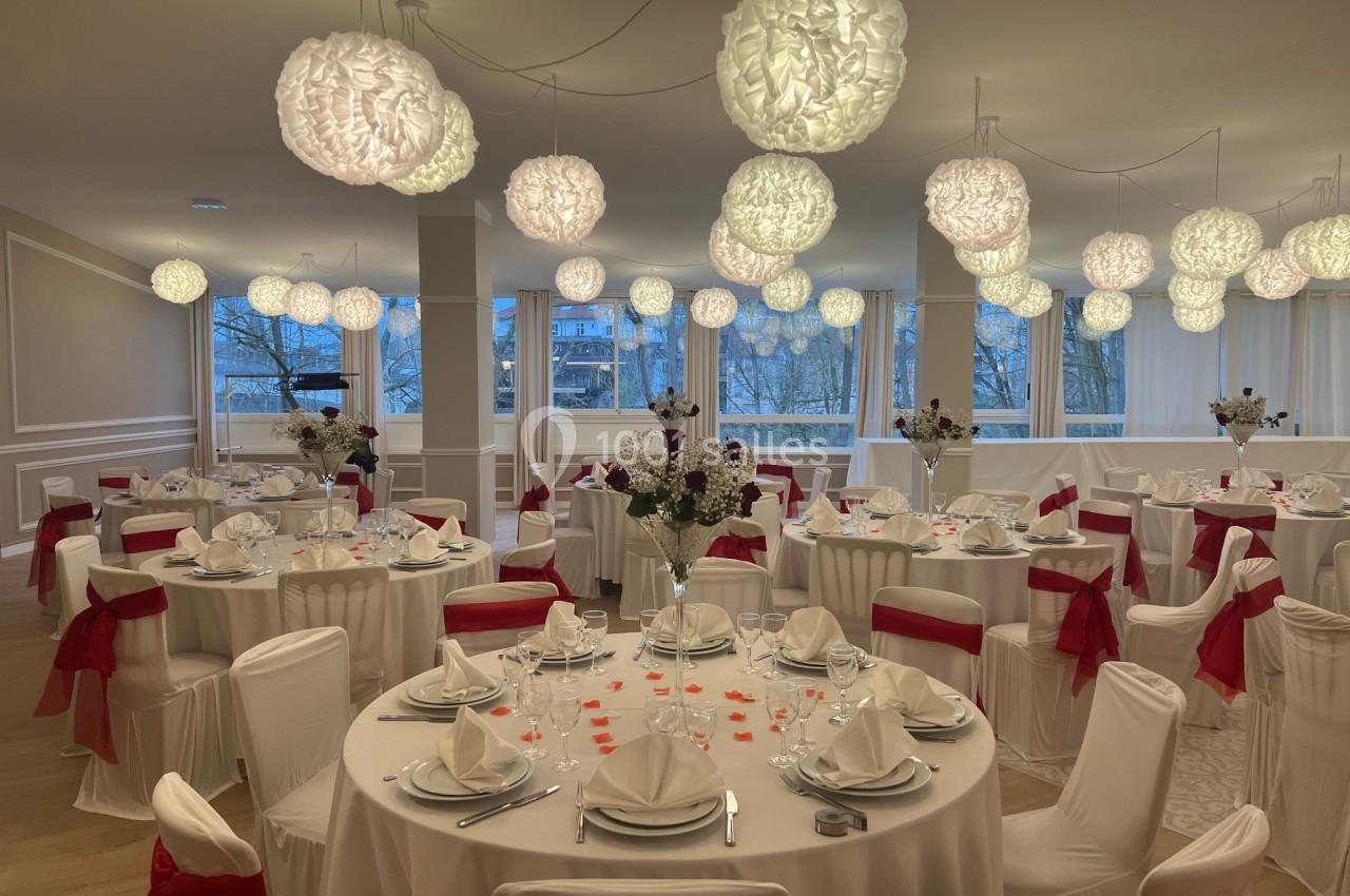 Salle de réception élégamment décorée avec des tables dressées, des chaises ornées de nœuds rouges et des luminaires…