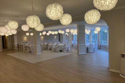 Salle lumineuse avec une grande table rectangulaire dressée, entourée de chaises décorées, parquet clair et fenêtres donnant…