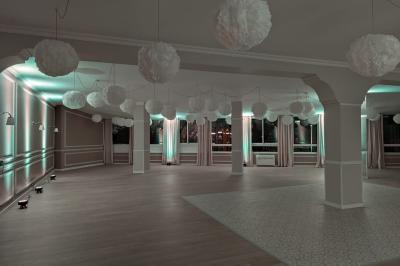 Salle lumineuse avec une grande table rectangulaire dressée, entourée de chaises décorées, parquet clair et fenêtres donnant…