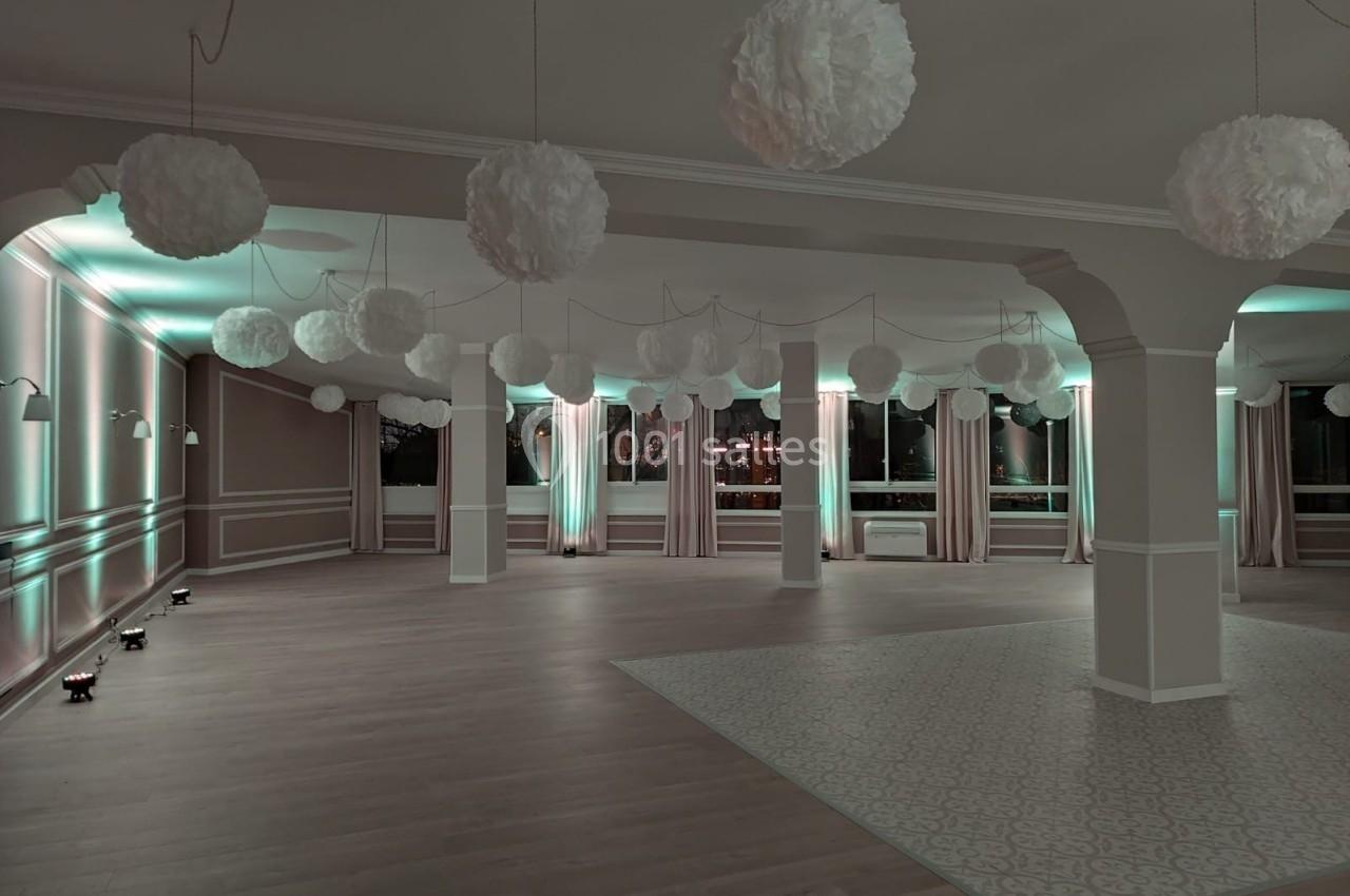 Salle vide décorée de suspensions blanches et éclairée par des lumières tamisées, avec parquet et carrelage au sol.