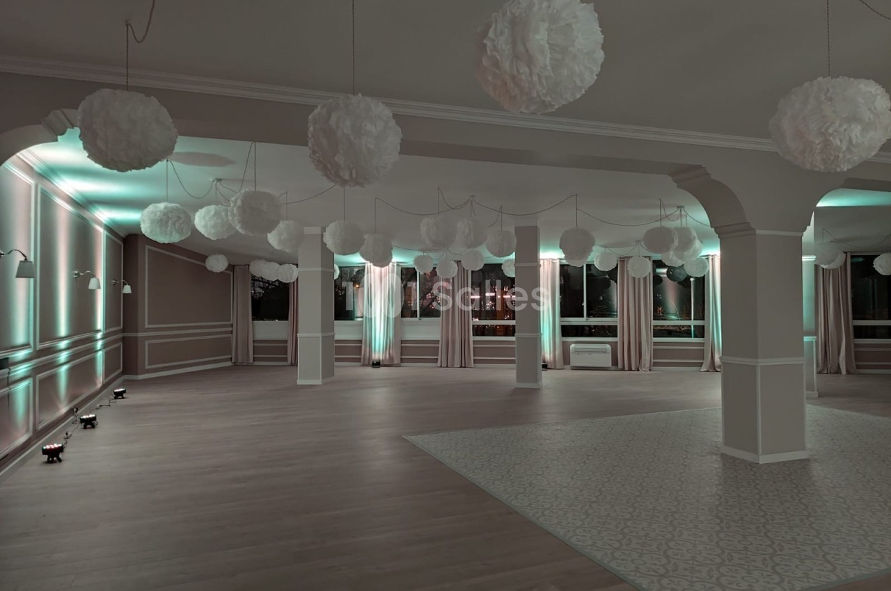 Salle vide décorée de suspensions blanches et éclairée par des lumières tamisées, avec parquet et carrelage au sol.