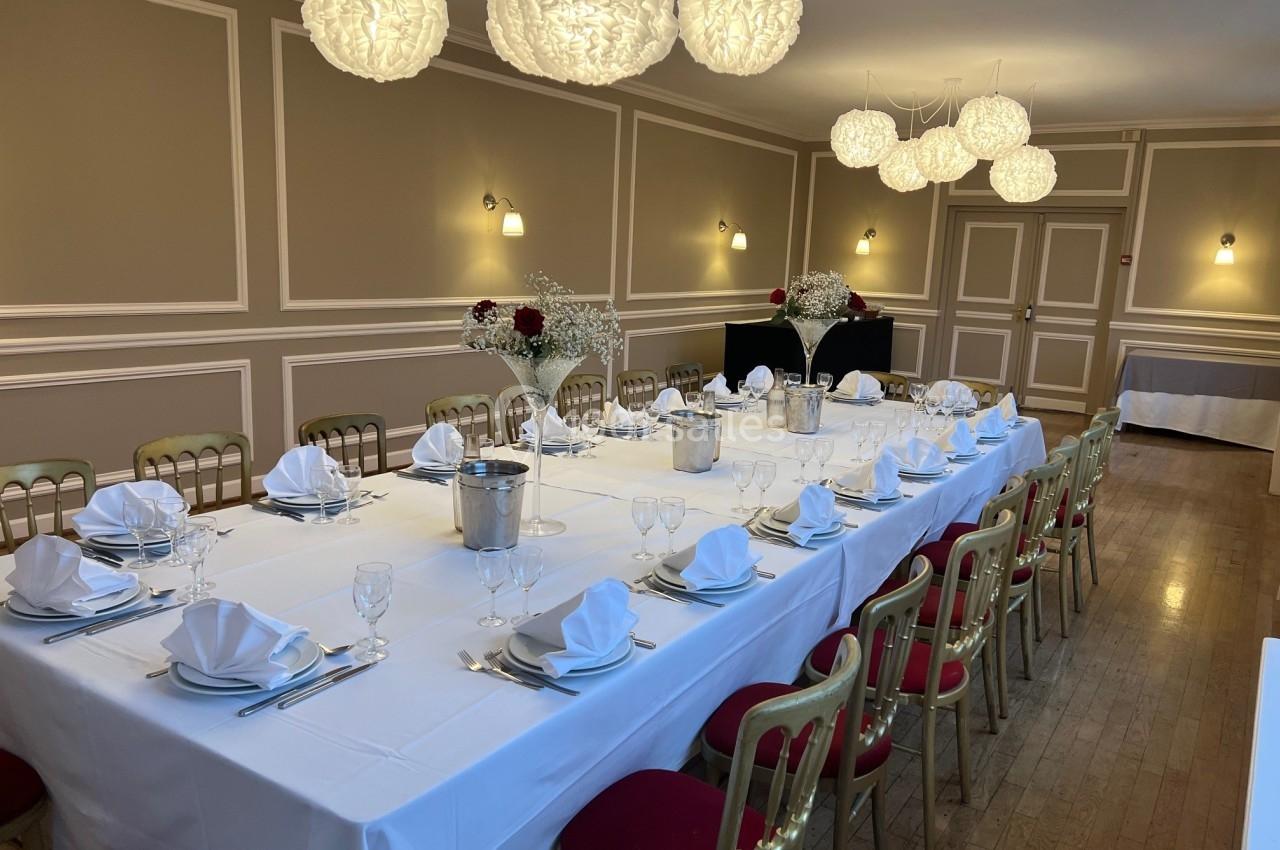 Salle élégante avec une grande table dressée pour un repas, décorée de fleurs et éclairée par des suspensions lumineuses.