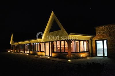 Miniature Location salle Cliponville (Seine-Maritime) - Le Clos Masure Simon #23 Bâtiment illuminé de nuit avec des façades vitrées et un toit en pente, entouré d'obscurité.