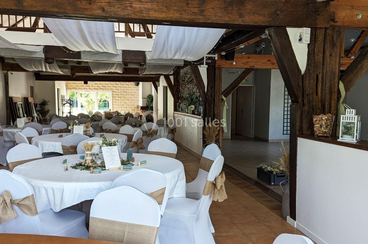 Salle de réception décorée avec des tables rondes, nappes blanches, chaises ornées de nœuds en toile de jute.