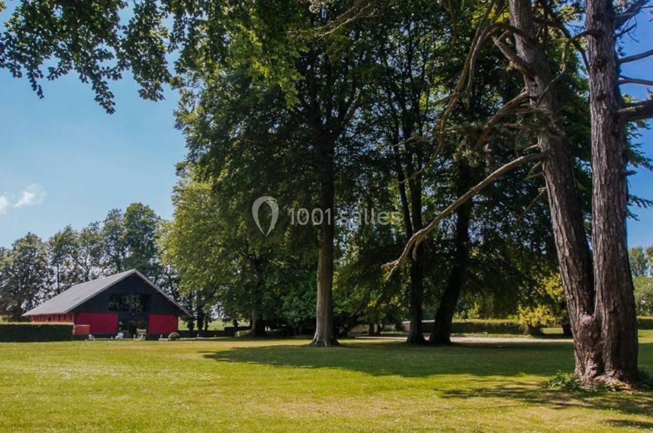 Un grand jardin verdoyant avec des arbres matures et une petite maison rouge en arrière-plan.