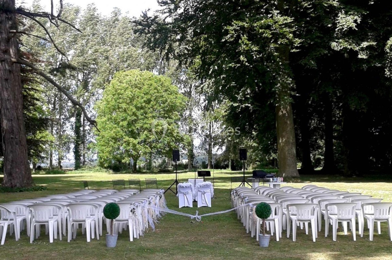 Chaises blanches disposées en rangées sur une pelouse, entourées d'arbres, avec un espace central décoré pour une cérémonie.
