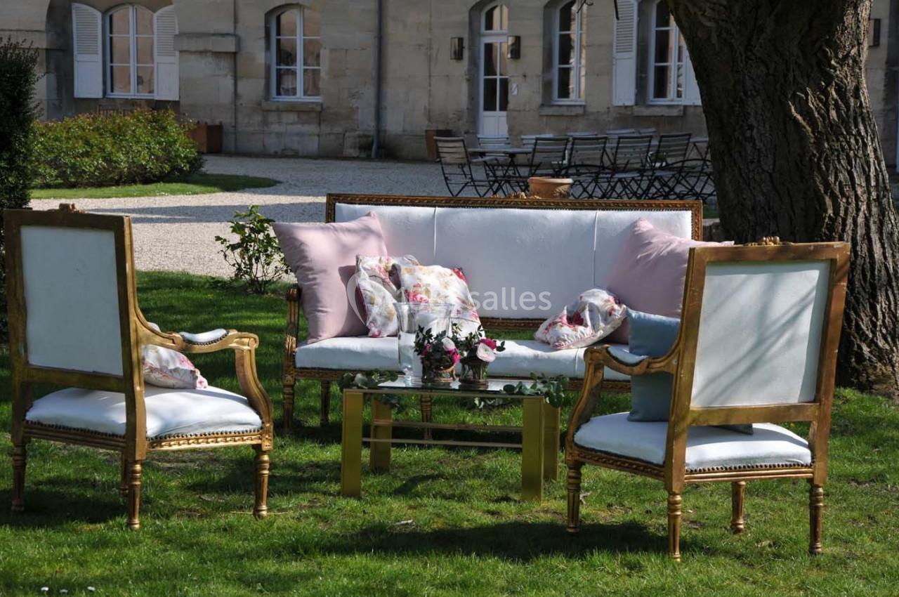 Mobilier de jardin élégant avec canapé et fauteuils dorés, disposé sur une pelouse près d'un bâtiment en pierre.