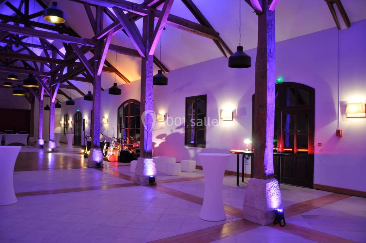 Salle spacieuse avec poutres apparentes, éclairage coloré et mobilier de réception moderne.