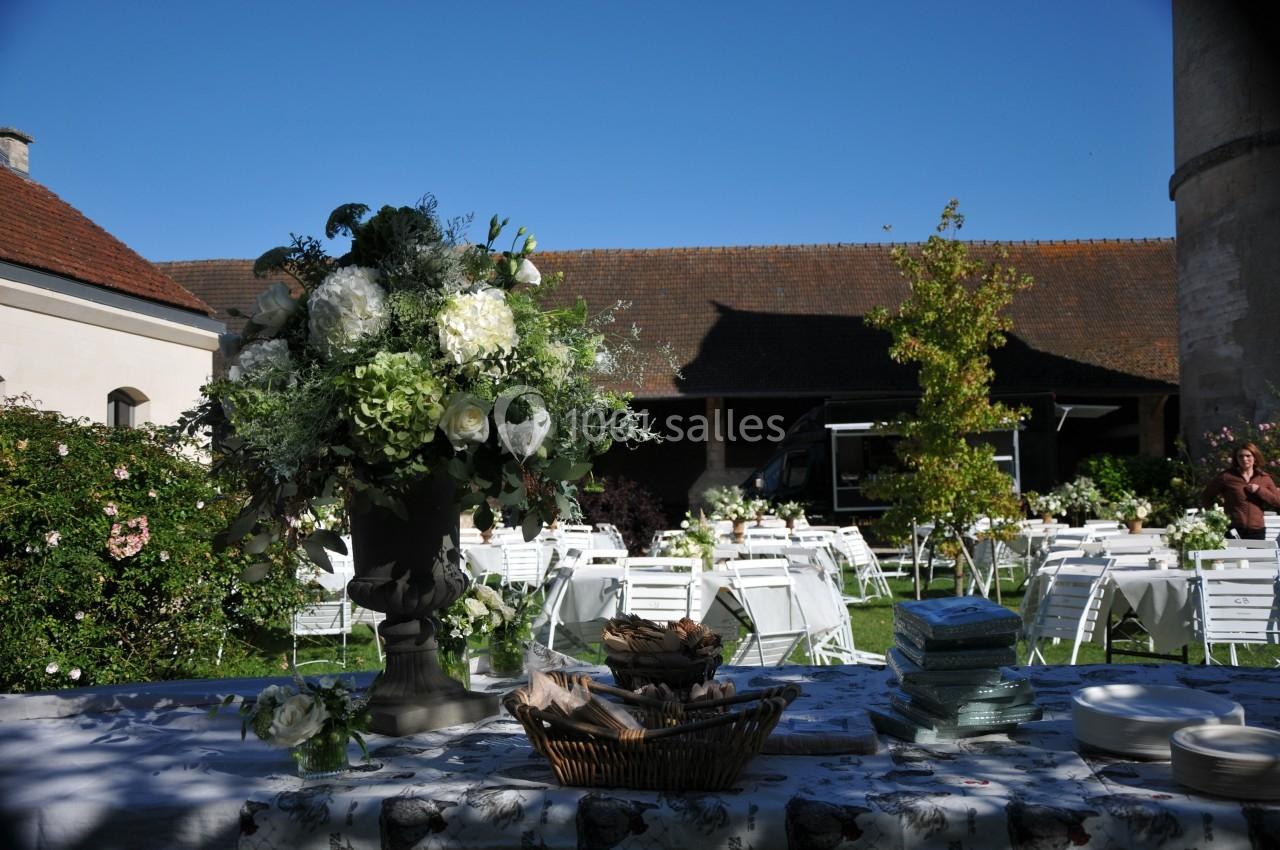 Arrangement floral sur une table décorée, avec des chaises et tables blanches disposées dans un jardin ensoleillé.