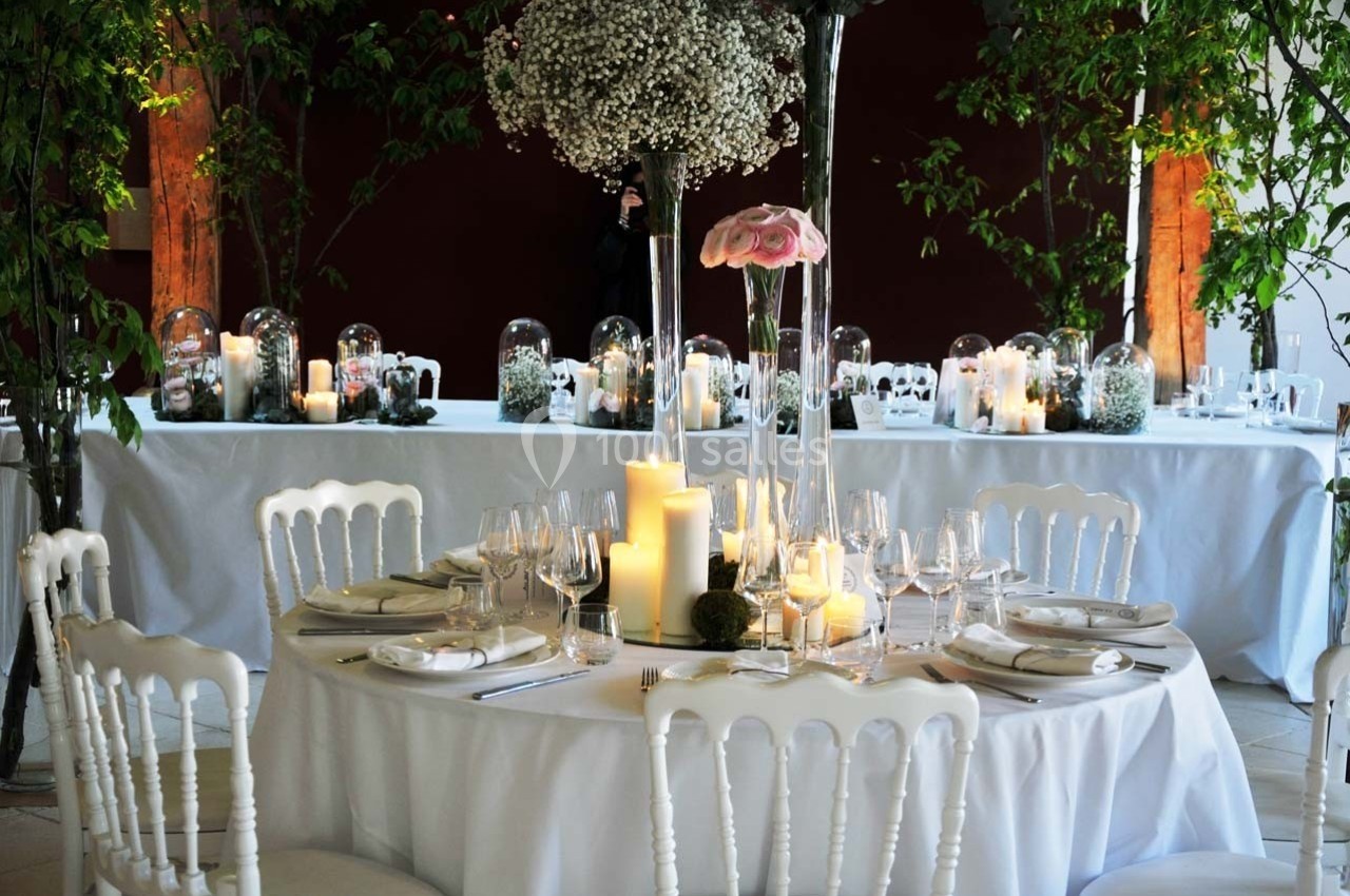 Table ronde décorée pour un événement, avec bougies, fleurs et vaisselle élégante, entourée de chaises blanches.