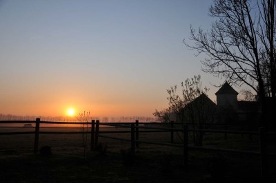Miniature Location salle Saint-Vaast-lès-Mello (Oise) - Le Clos Barisseuse #33 Cour enneigée avec bâtiments en pierre, un pigeonnier cylindrique et des arbres nus sous un ciel dégagé.