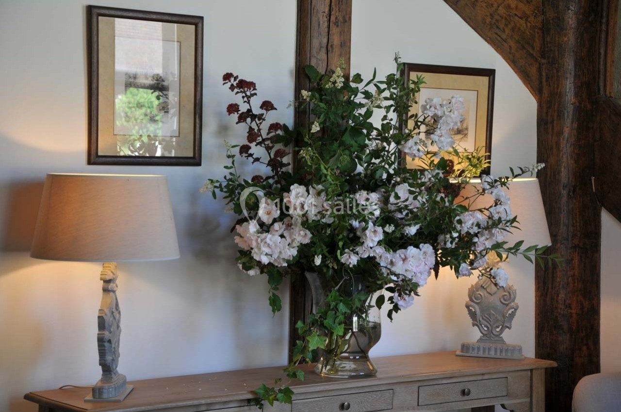 Vase de fleurs blanches et rouges sur une console en bois, encadré par deux lampes et des tableaux au mur.