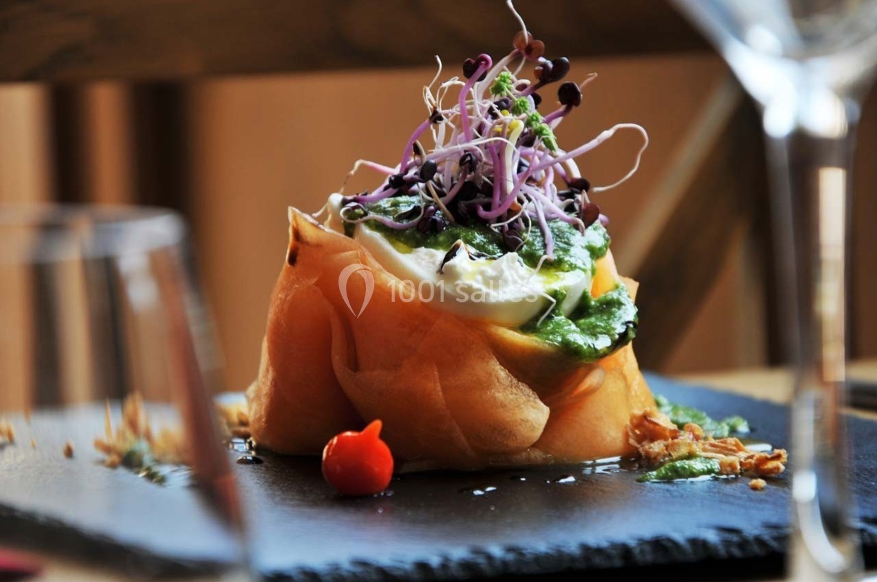 Plat raffiné composé d'une pâte croustillante garnie de crème, légumes verts et pousses, présenté sur une ardoise.