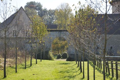 Miniature Location salle Saint-Vaast-lès-Mello (Oise) - Le Clos Barisseuse #30 Cour enneigée avec bâtiments en pierre, un pigeonnier cylindrique et des arbres nus sous un ciel dégagé.