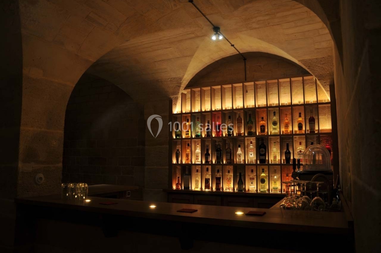 Bar en pierre voûtée avec étagères éclairées exposant des bouteilles d'alcool, ambiance tamisée et chaleureuse.