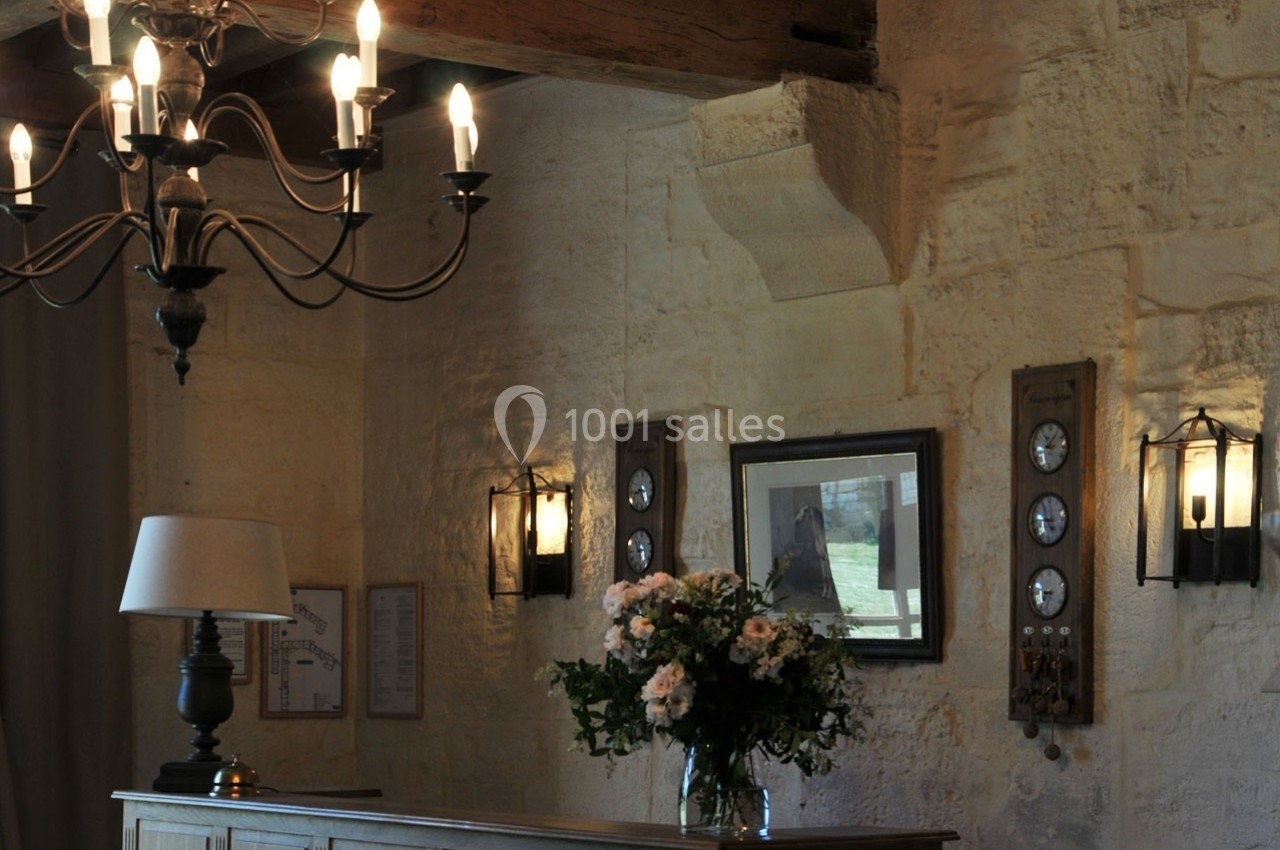 Intérieur rustique avec murs en pierre, lustre, lampe, bouquet de fleurs et instruments muraux décoratifs.