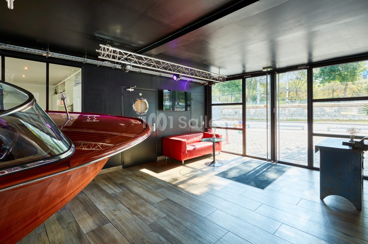 Intérieur lumineux avec un bateau en bois, un canapé rouge et de grandes baies vitrées donnant sur l'extérieur.
