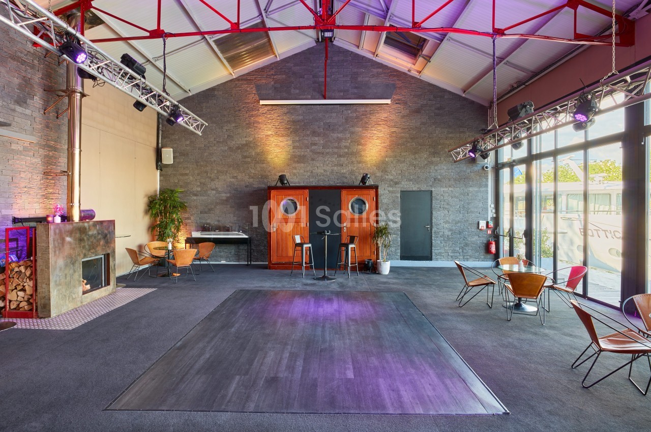 Salle spacieuse avec parquet central, murs en pierre, mobilier moderne et éclairage coloré, ambiance industrielle.