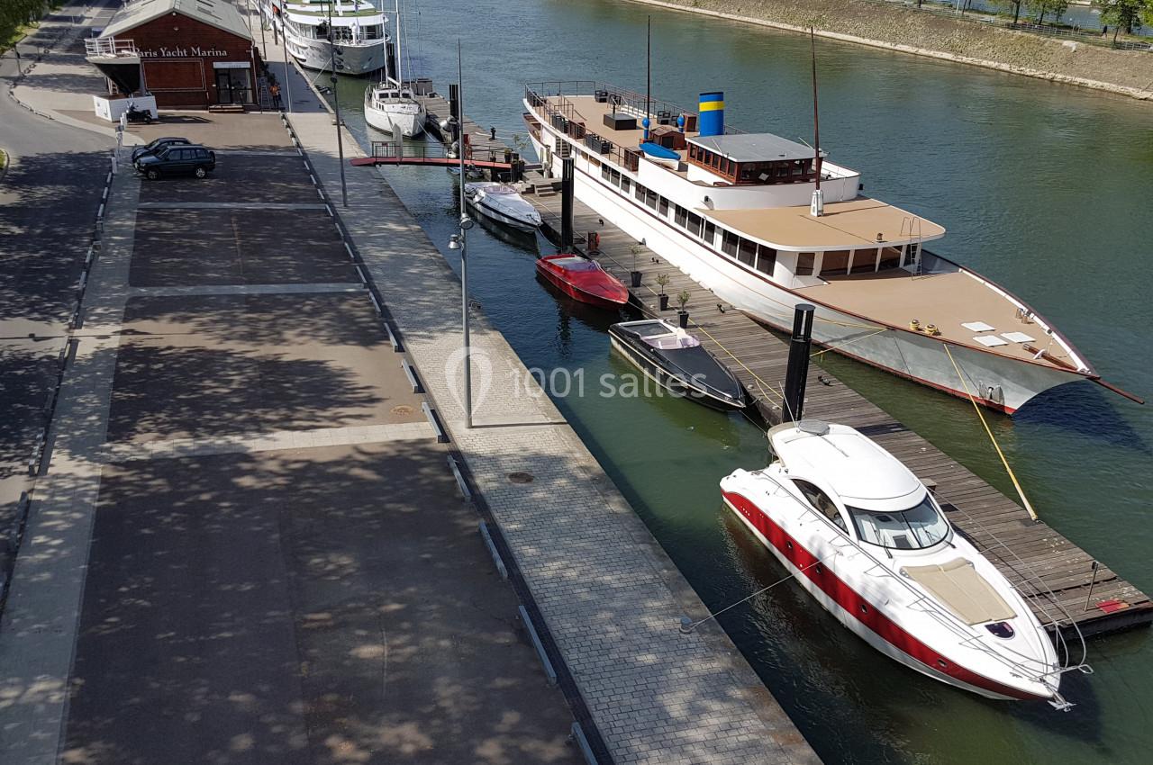 Bateaux amarrés le long d'un quai sur une rivière, avec une promenade bordée d'arbres à gauche.