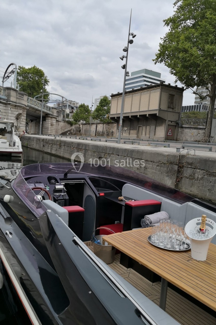 Bateau amarré le long d'un quai, avec une table dressée et des bâtiments en arrière-plan.