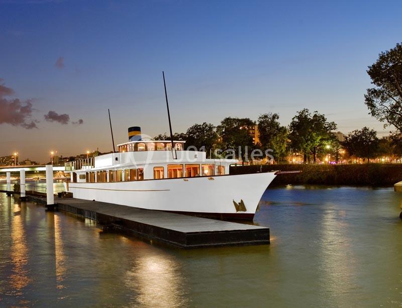 Bateau blanc amarré à un quai au crépuscule, entouré d'arbres et d'eau calme.