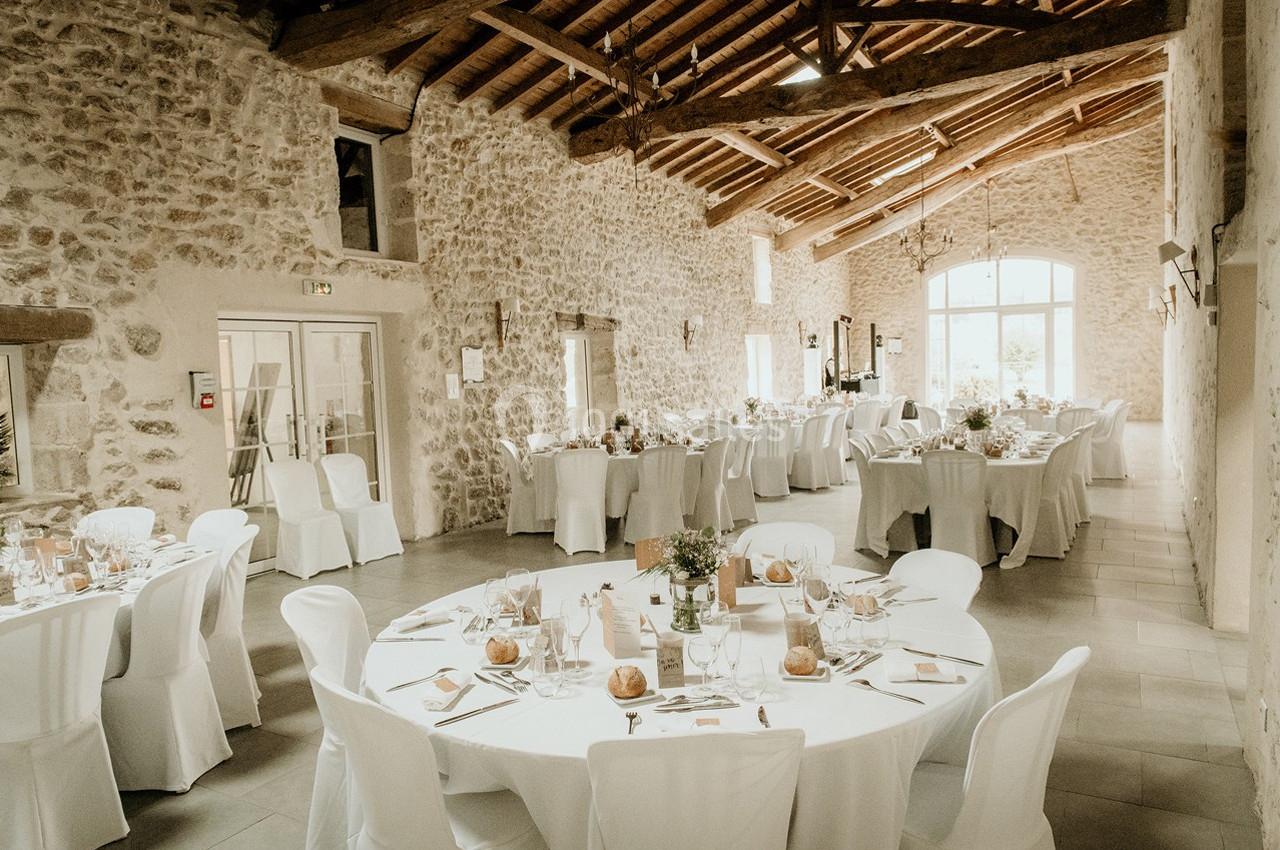 Salle de réception en pierre avec tables rondes et rectangulaires dressées pour un événement festif.