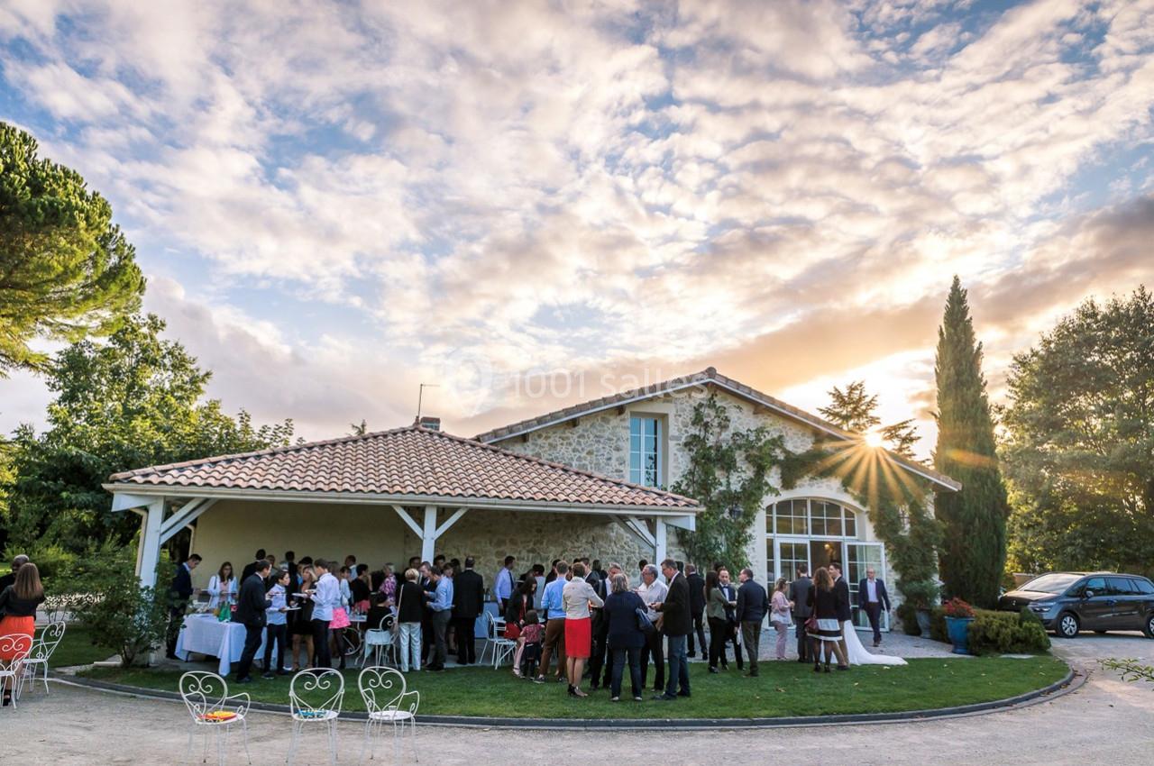 Groupe de personnes réunies devant une maison en pierre au coucher du soleil, entourée de verdure.