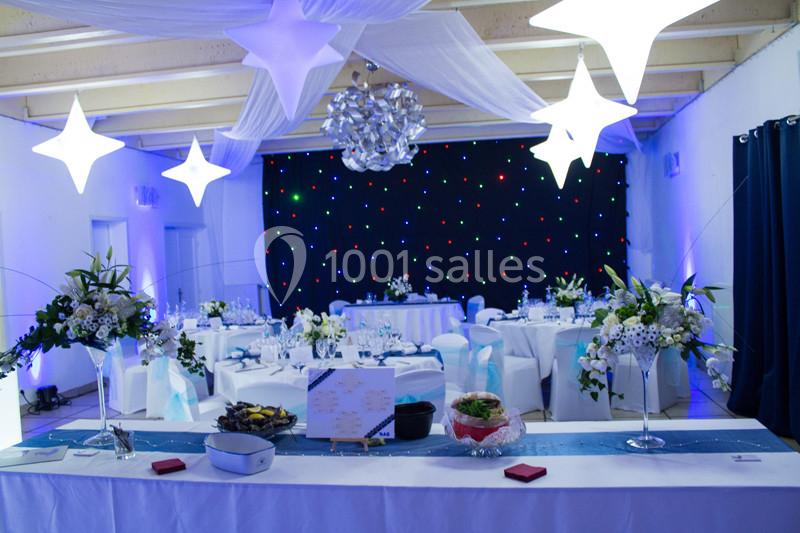Salle de réception décorée avec des tables dressées, des fleurs, des lumières suspendues et un fond étoilé lumineux.