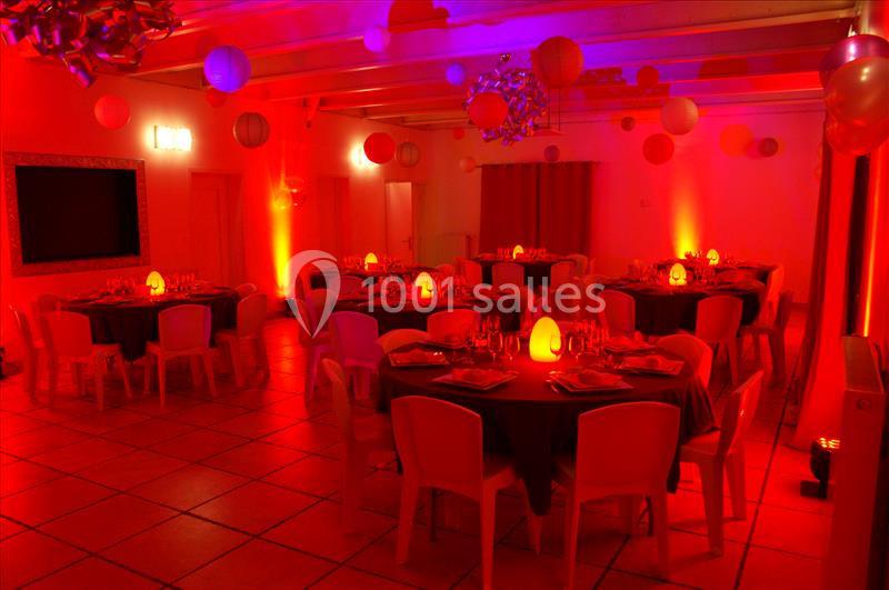 Salle de réception éclairée en rouge avec des tables rondes dressées et des décorations suspendues.
