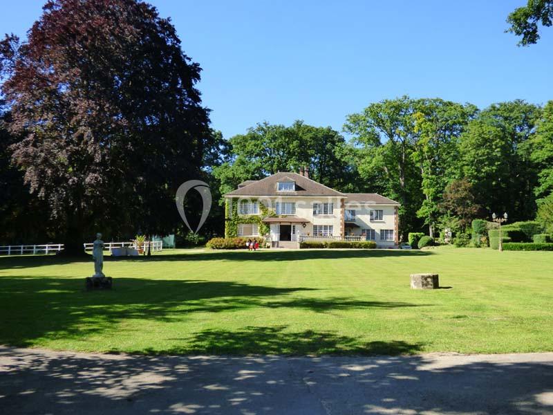 Grande maison entourée d'un vaste jardin verdoyant avec des arbres et une pelouse bien entretenue sous un ciel bleu.