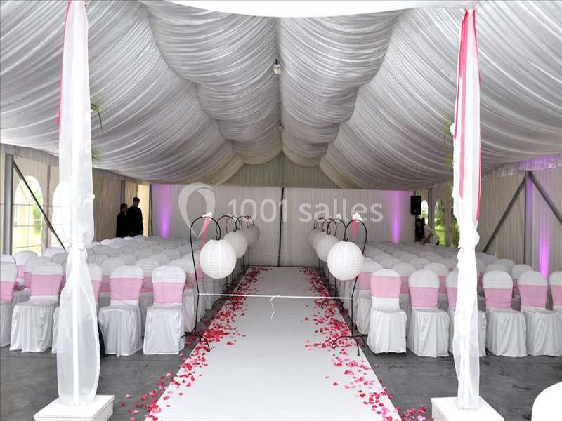 Salle de réception décorée avec des chaises blanches et roses, allée centrale ornée de pétales rouges et lanternes…