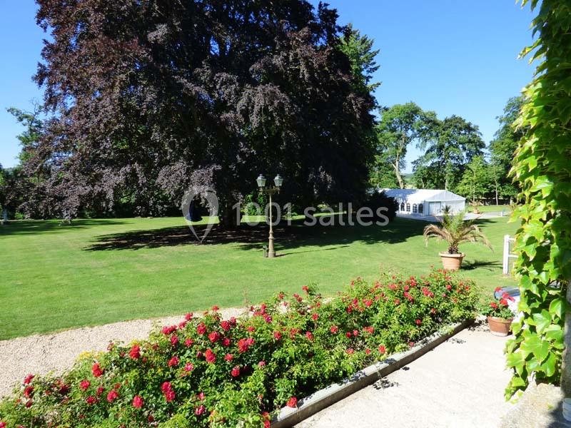 Jardin avec pelouse, parterre de roses, grand arbre, lampadaire et tente blanche en arrière-plan par temps ensoleillé.