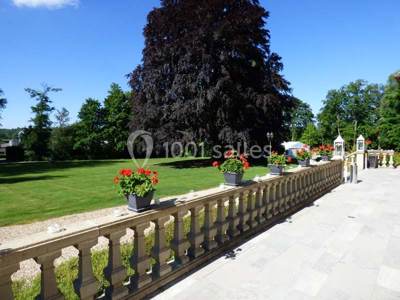 Terrasse en pierre avec balustrade ornée de jardinières fleuries, donnant sur un grand jardin verdoyant et arboré.